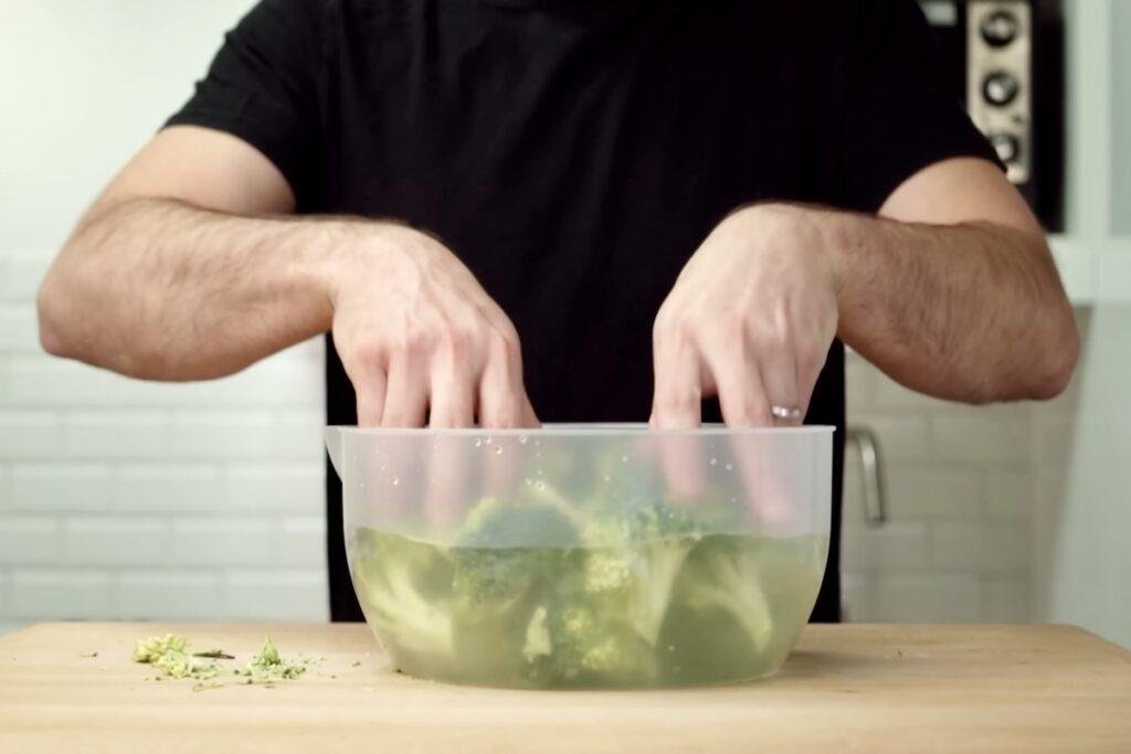 Broccoli florets soaking in a clear bowl of salted water
