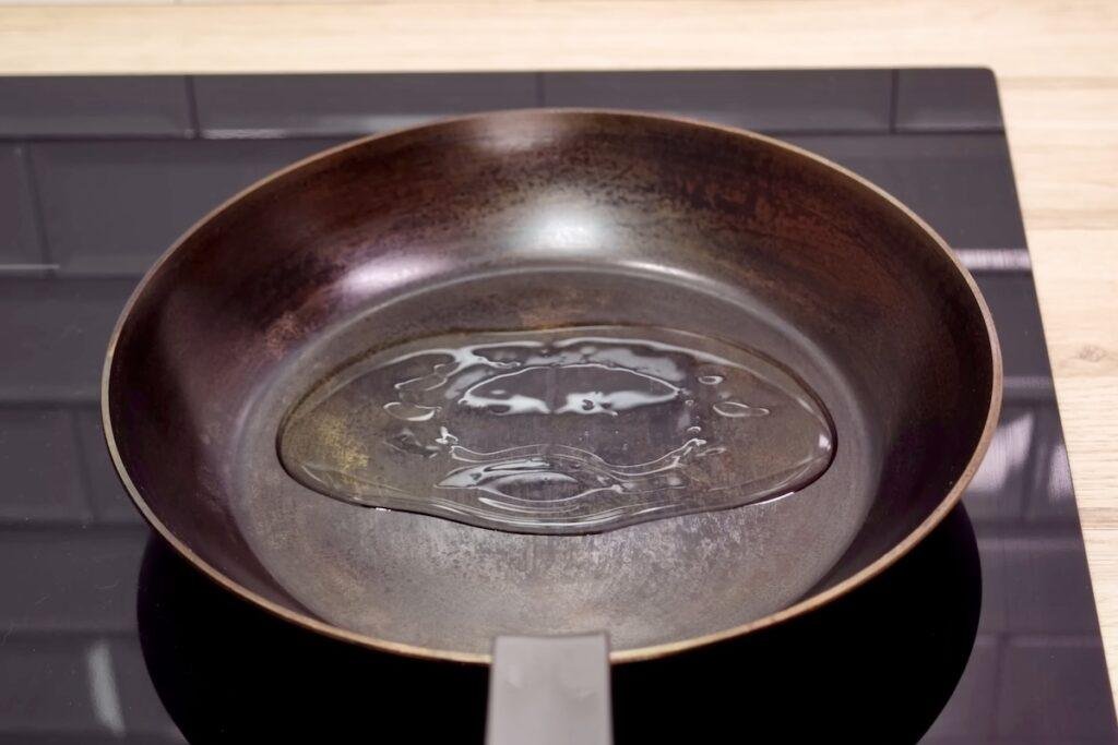 Olive oil coating the base of an empty heavy frying pan on an induction hob