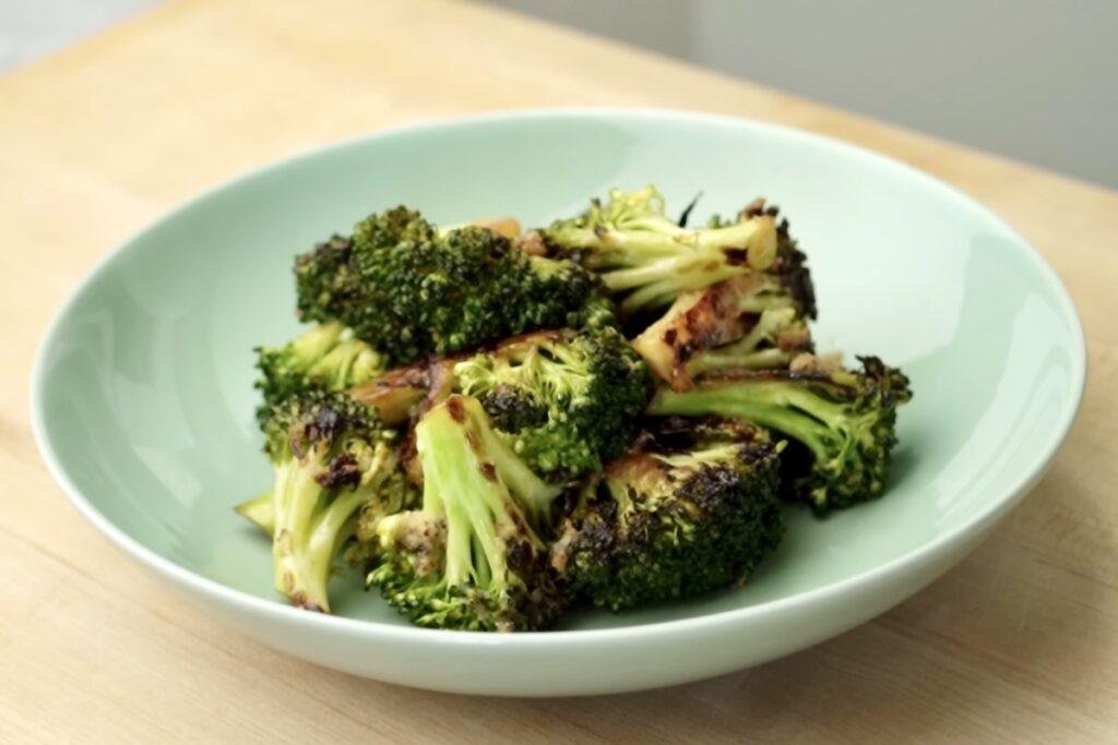 Pan roasted broccoli florets with charred edges served in a pale green bowl on a wooden table