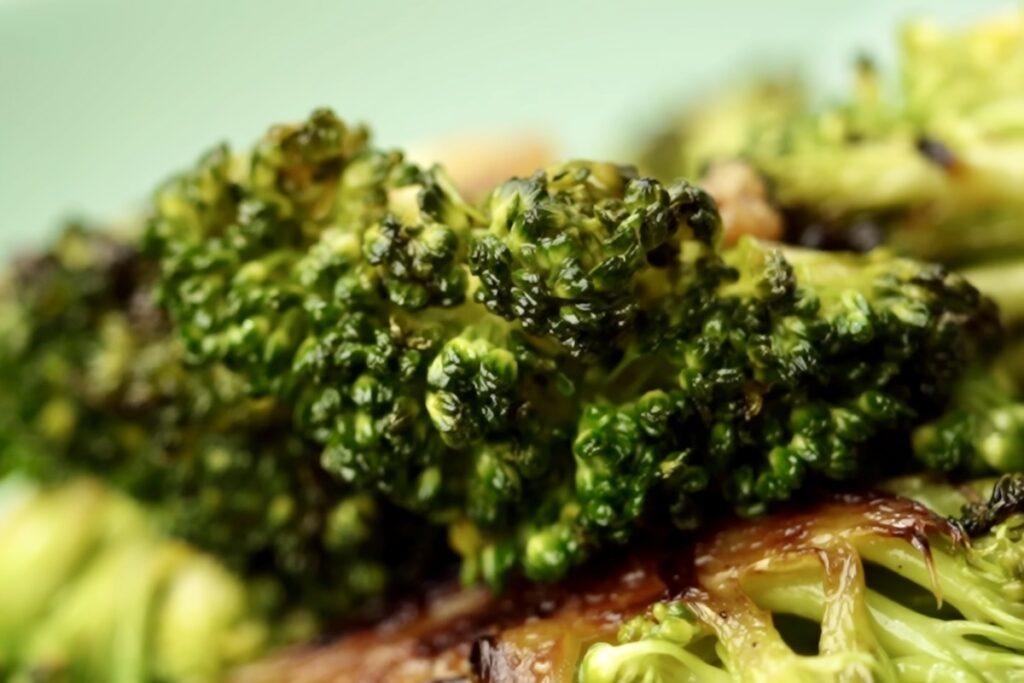 Close up of bright green pan roasted broccoli florets with charred edges on a pale green plate