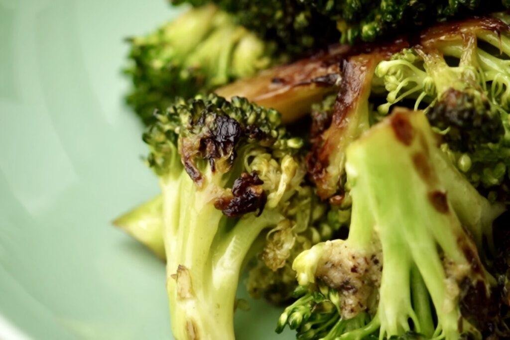 Charred broccoli pieces with browned cut sides and green florets on a pale green plate