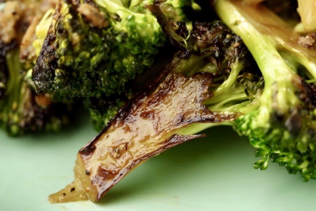 Broccoli stalk with a deeply charred cut side lying among green florets on a pale green plate