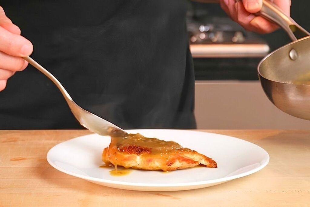 Spoon pouring pan sauce over a seared chicken breast on a white plate
