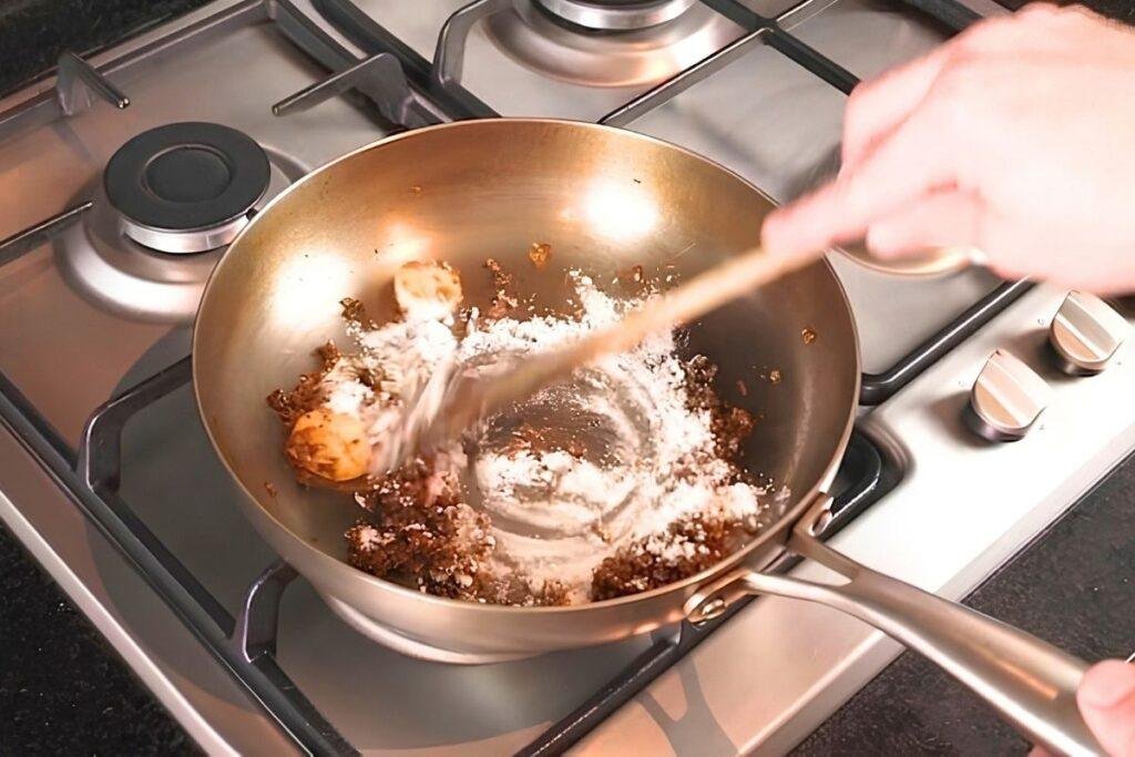 flour being added to a pan with onions and mushrooms