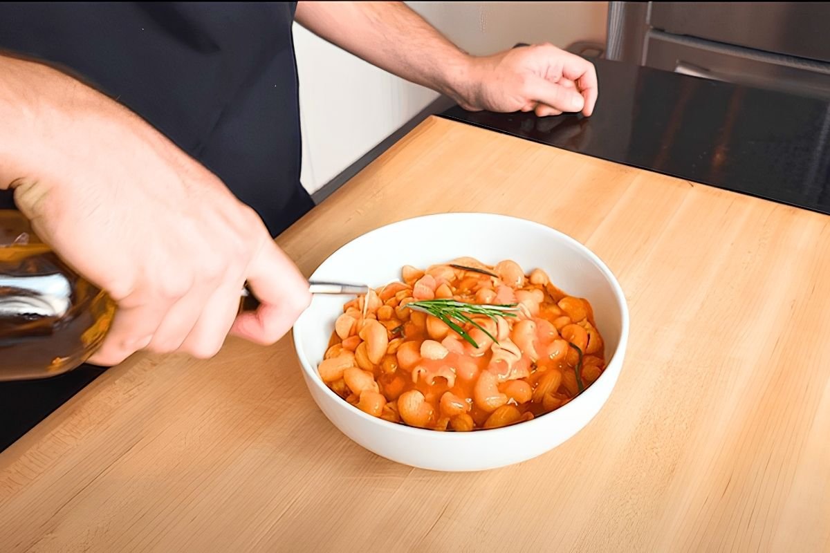 Olive oil being poured over a white bowl of pasta e ceci with a rosemary sprig