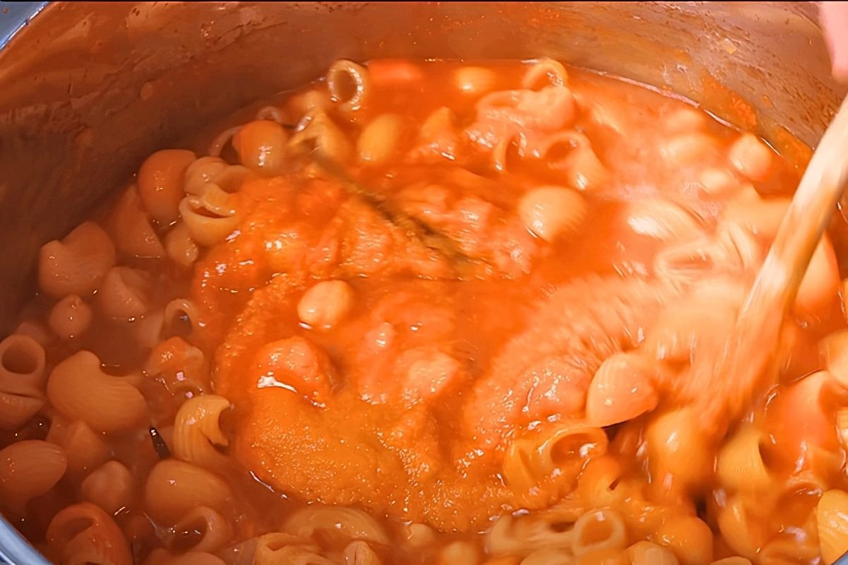Wooden spoon stirring pasta into a tomato and chickpea sauce in a steel pot