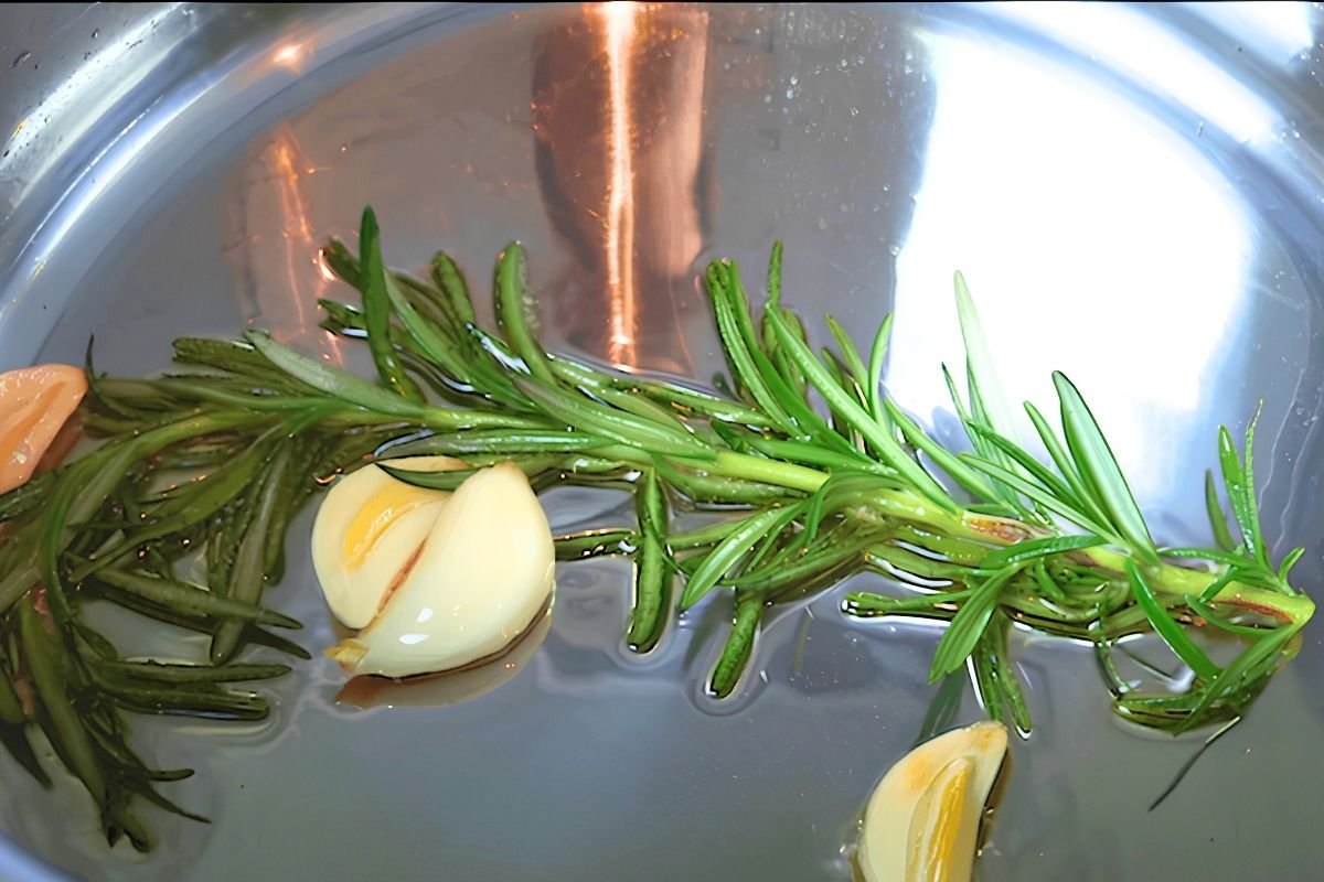 Rosemary sprig and garlic cloves sizzling in olive oil in a steel pan