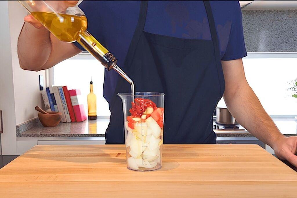 Olive oil being poured into a tall jug of ingredients for aioli