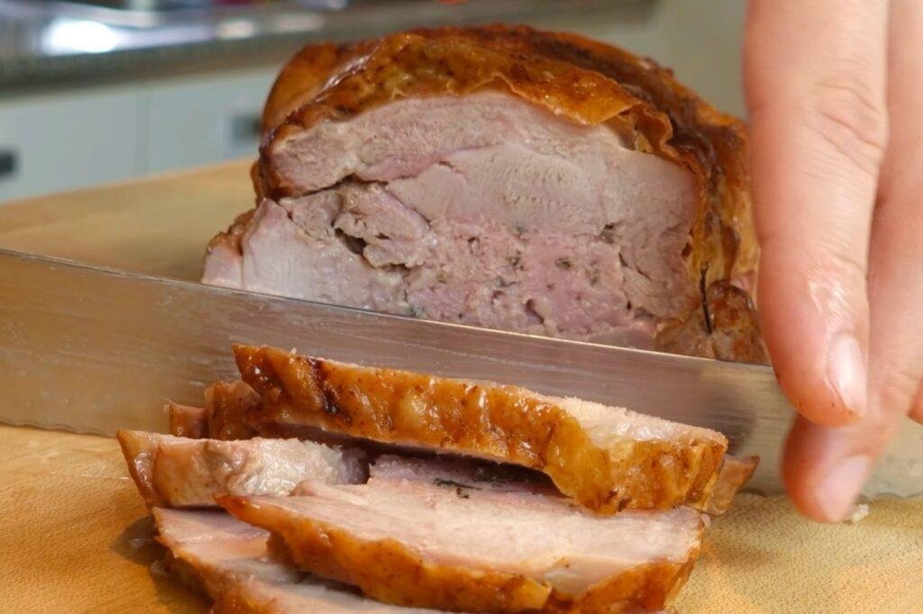 Knife carving a golden roasted rolled turkey joint on a wooden board