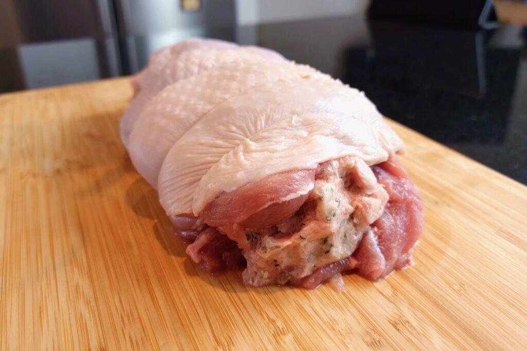 Raw rolled turkey joint with skin wrapped around the meat on a wooden board