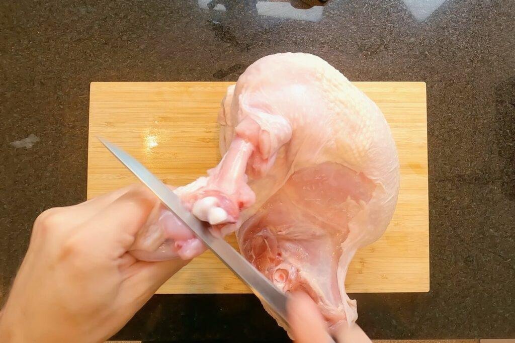 Overhead view of a knife cutting into a raw turkey on a wooden board