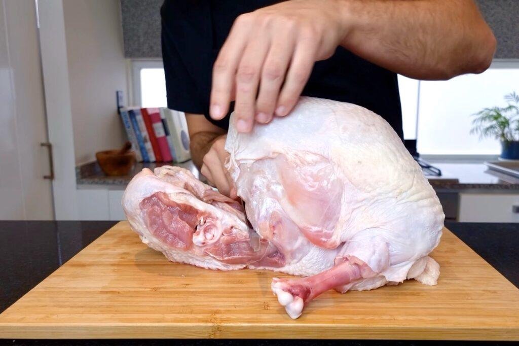 Hand resting on a raw turkey crown beside boned turkey meat on a wooden board