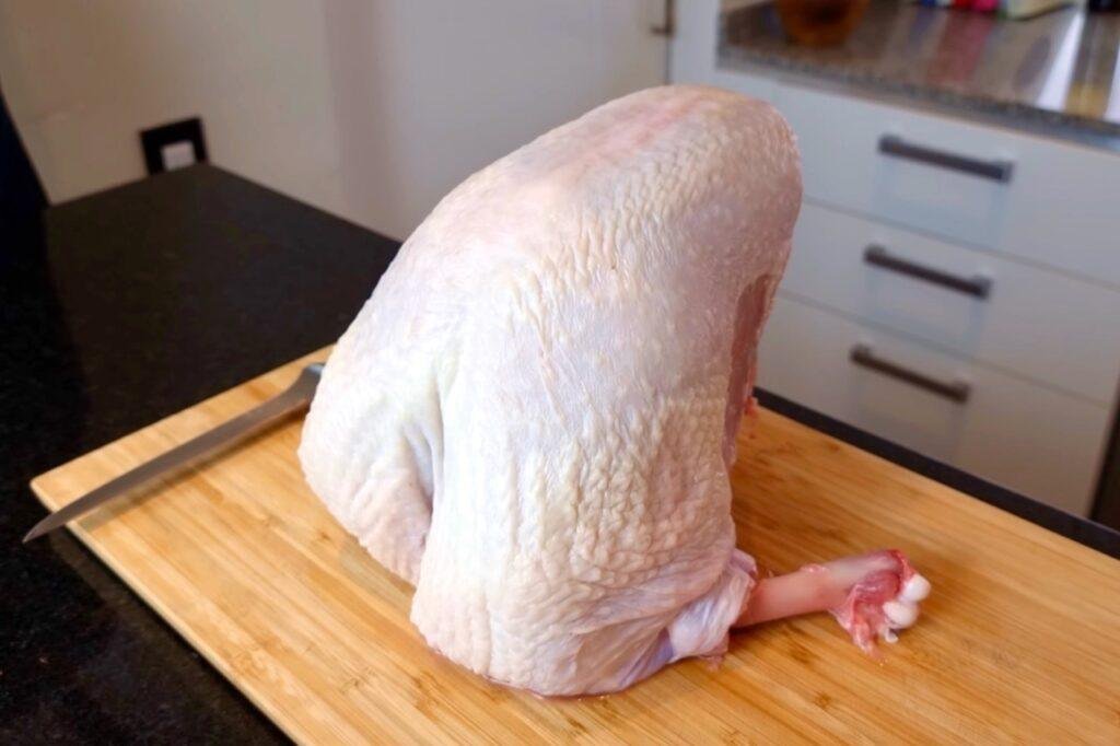 Raw turkey crown on a wooden board with a knife beside it
