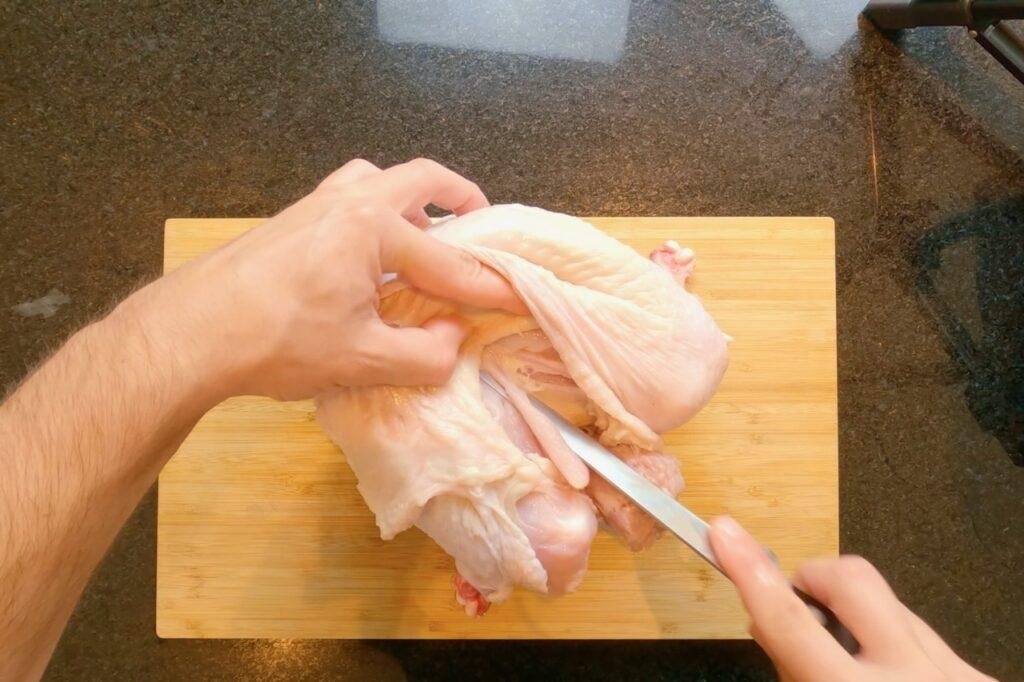 Overhead view of hands cutting raw turkey with a knife on a wooden board