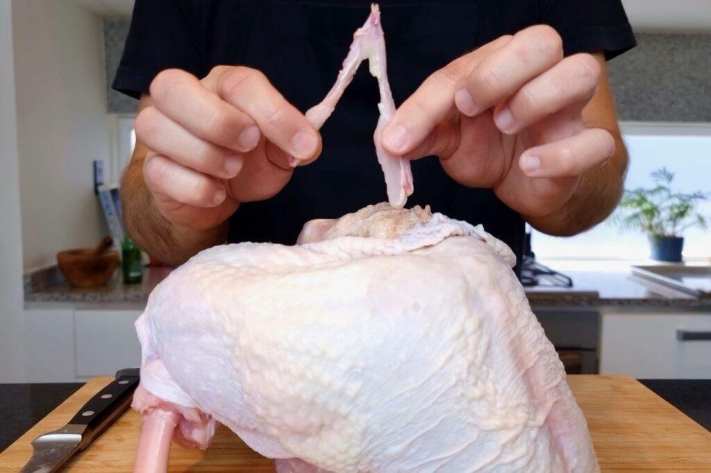 Hands pulling a white sinew from a raw turkey breast