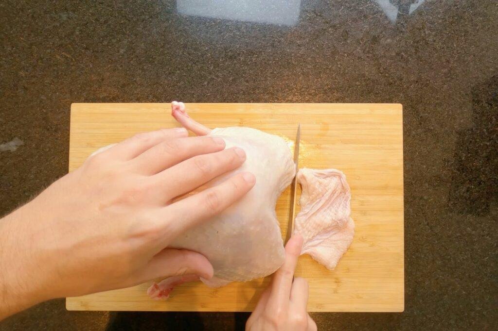 Overhead view of a knife trimming skin from a raw turkey breast on a wooden board