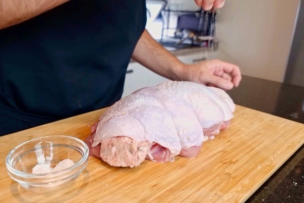 Raw turkey breast sliced into sections on a wooden board beside a small bowl of salt