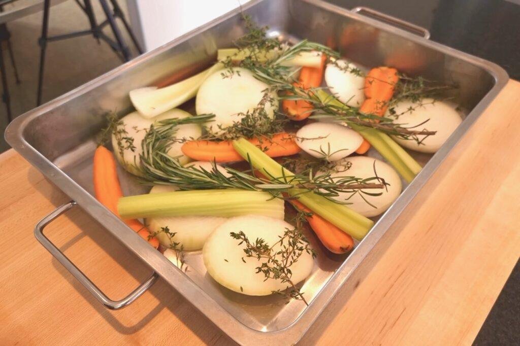 Roasting tin of onion, carrot, celery and herbs on a wooden counter