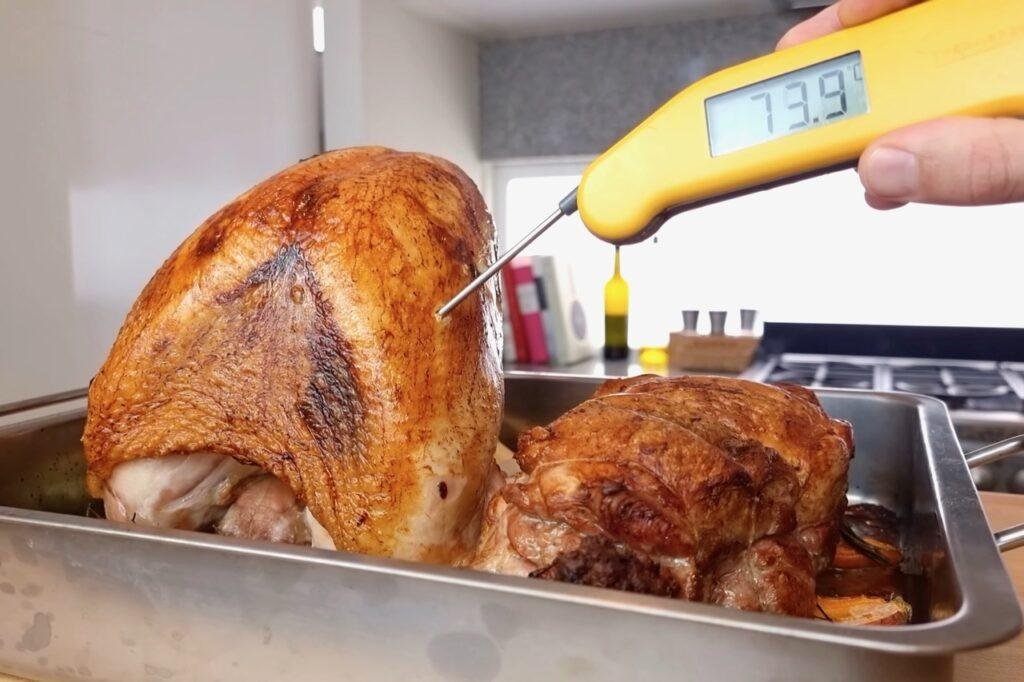 Yellow digital thermometer probing a golden roast turkey crown in a roasting tin