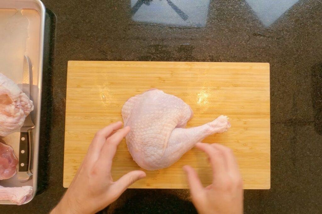 Overhead view of hands holding a raw turkey leg on a wooden board