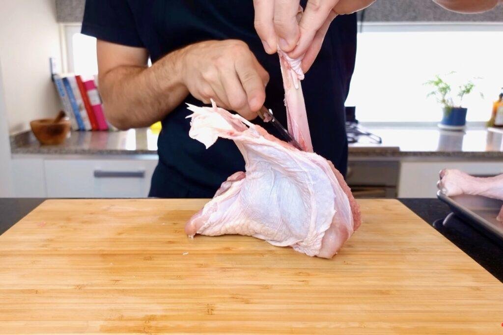 Person peeling skin back from a raw turkey leg on a wooden board