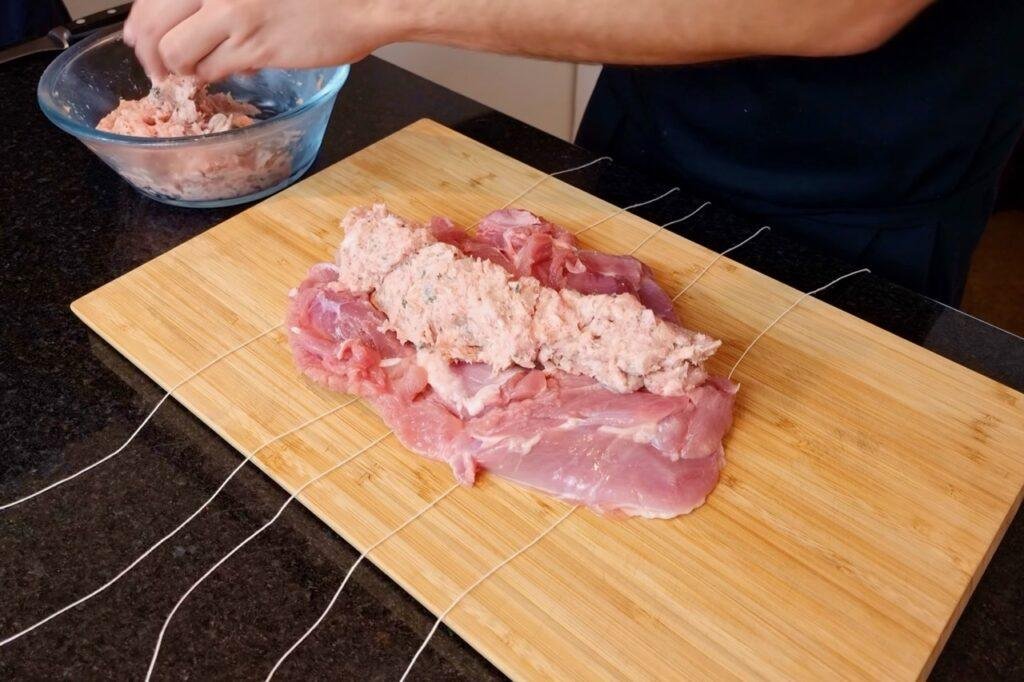 Raw boned turkey thigh with stuffing spread on top, string laid beneath and a bowl of stuffing beside it