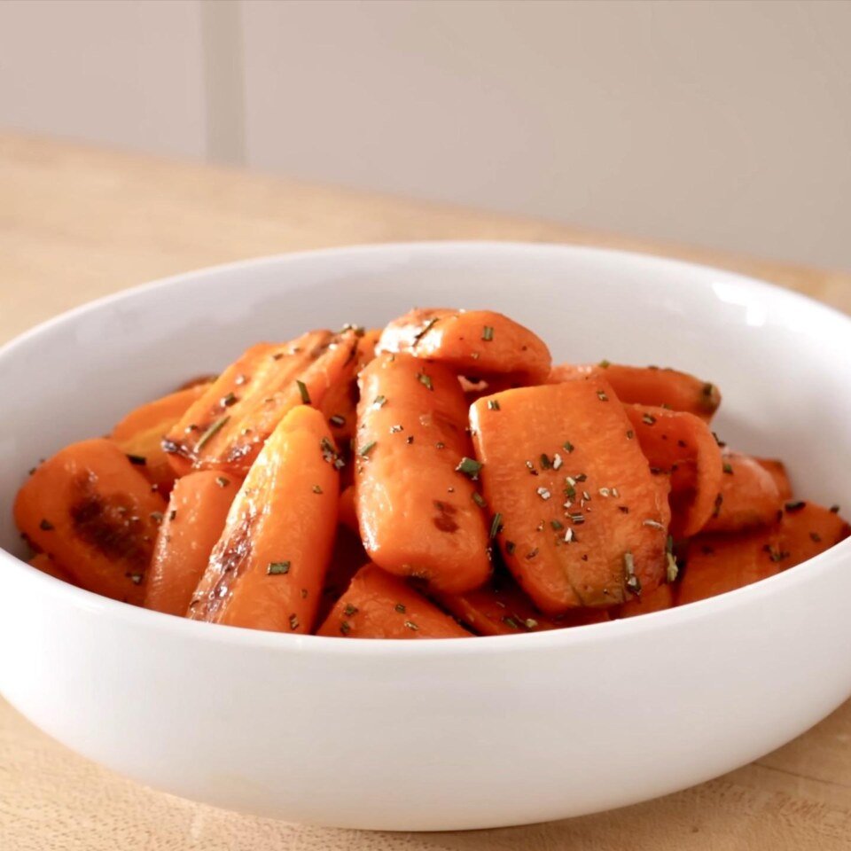 White bowl of glazed roasted carrot pieces with herbs on a wooden counter