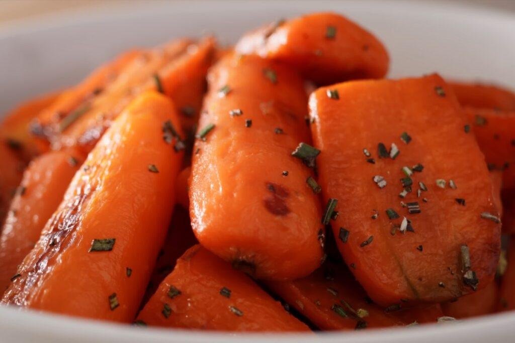 Glossy roasted carrots sprinkled with chopped rosemary in a white bowl