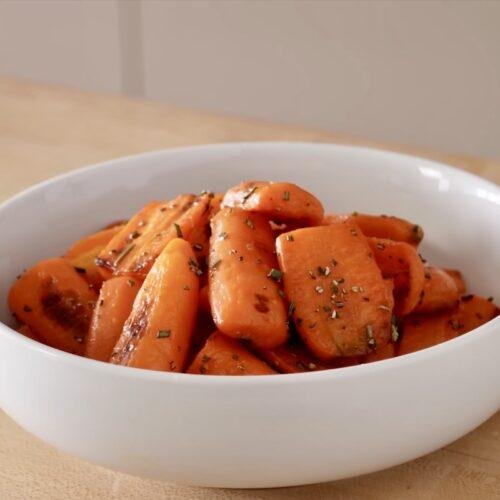 White bowl of glazed roasted carrots sprinkled with fresh herbs