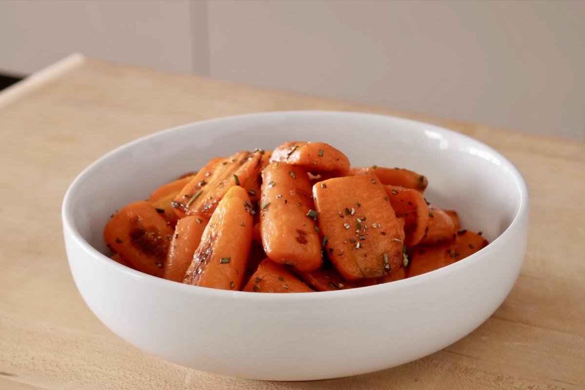 White bowl of glazed roasted carrots sprinkled with fresh herbs