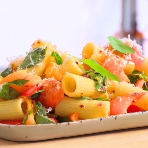 Rigatoni pasta salad with roasted peppers, basil and parmesan on a ceramic platter