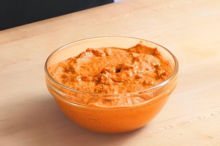 Glass bowl of orange romesco sauce on a wooden board