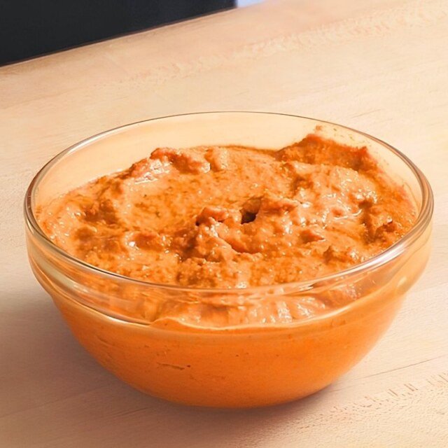 Glass bowl of orange romesco sauce on a wooden board