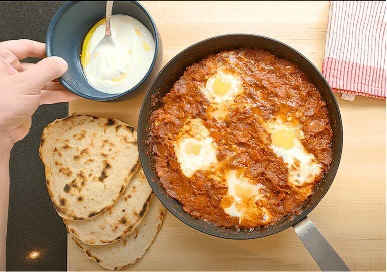 Shakshuka in a pan with flatbreads and a small bowl of yoghurt