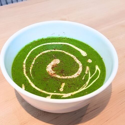 Green spinach soup in a white bowl with a creamy swirl, seen from above on a wooden board