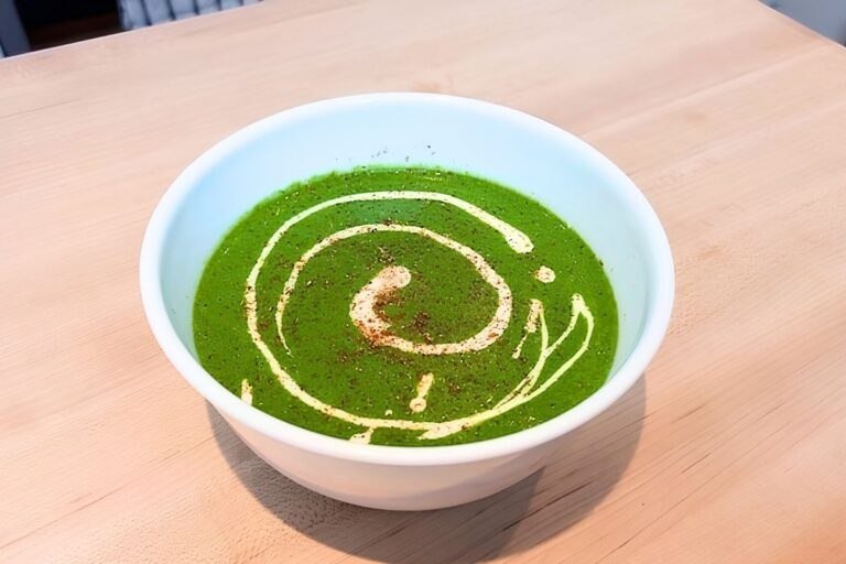 Green spinach soup in a white bowl with a creamy swirl, seen from above on a wooden board