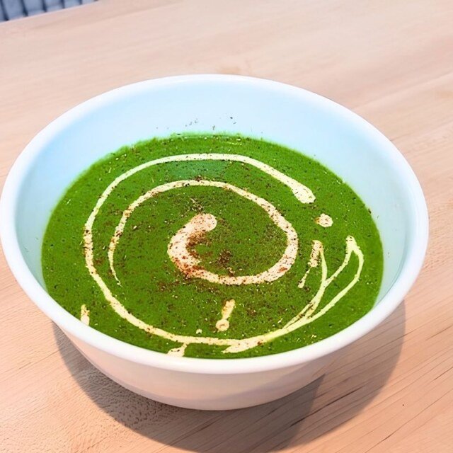 Green spinach soup in a white bowl with a creamy swirl, seen from above on a wooden board