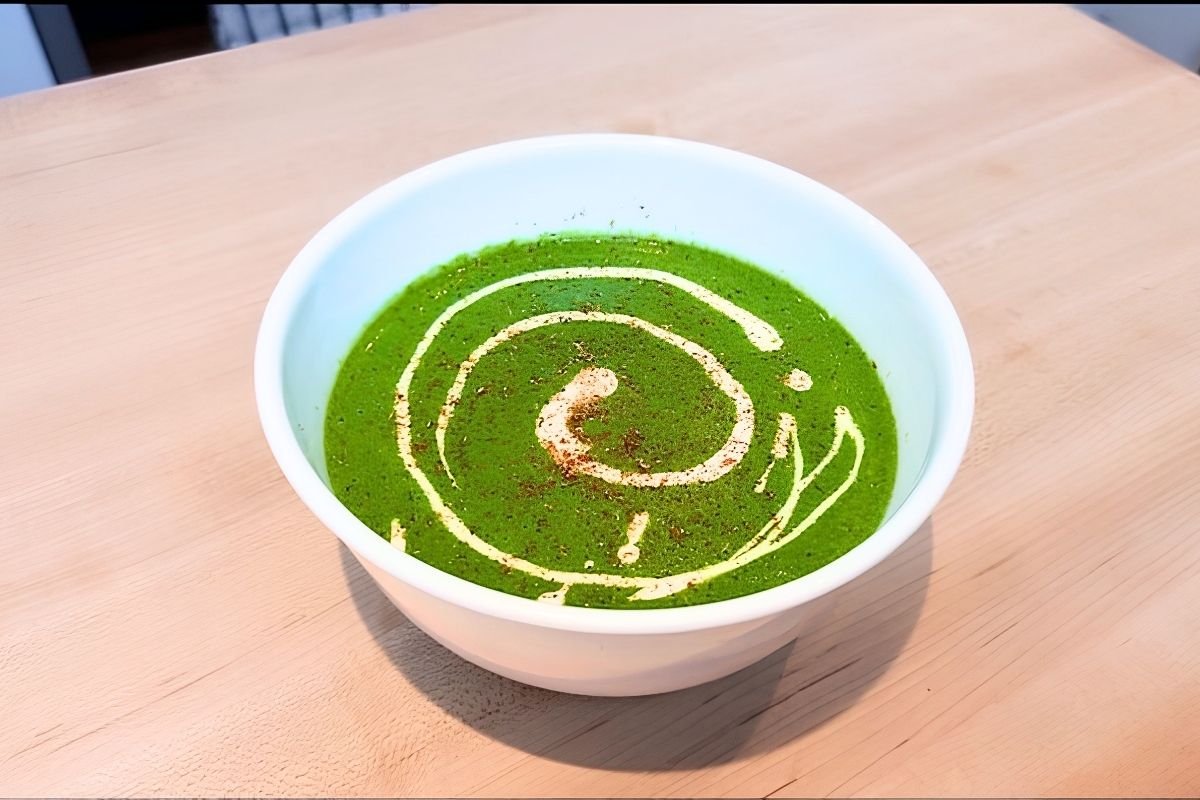 White bowl of green spinach and potato soup topped with a spiral of cream and a sprinkle of ground spice