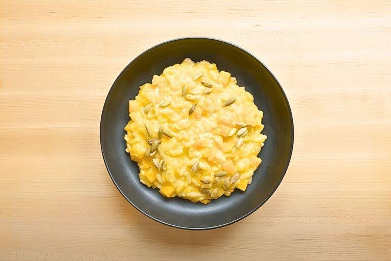 Dark bowl of butternut squash orzo topped with pumpkin seeds, seen from above