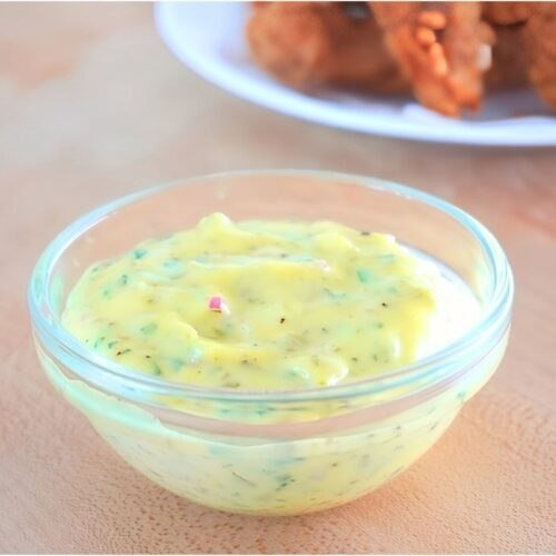 Small glass bowl of tartar sauce with a plate of fried chicken in the background