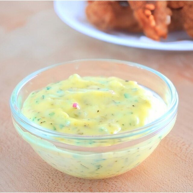 Small glass bowl of tartar sauce with a plate of fried chicken in the background