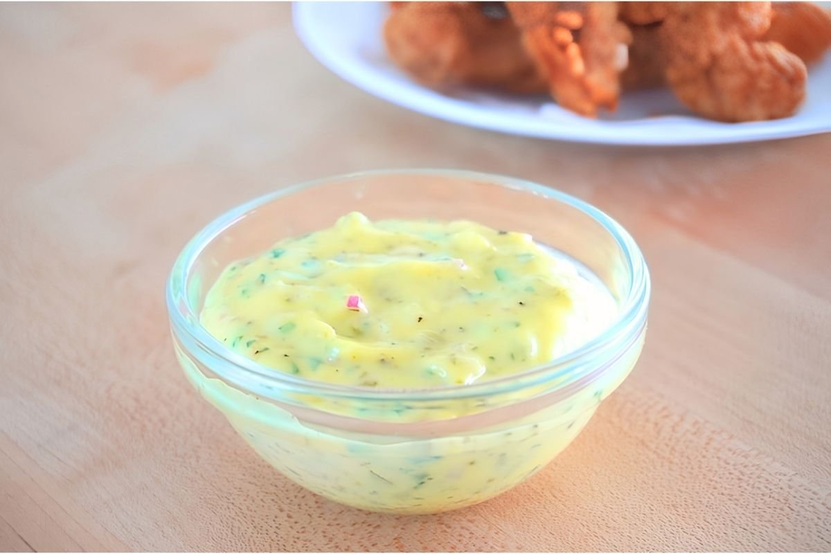 Small glass bowl of tartar sauce with a plate of fried chicken in the background