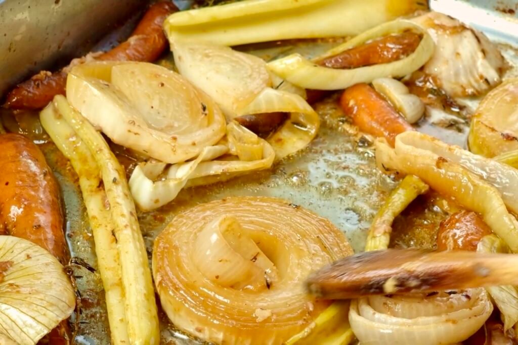 Close up of roasted onion and carrot pieces in a roasting tin