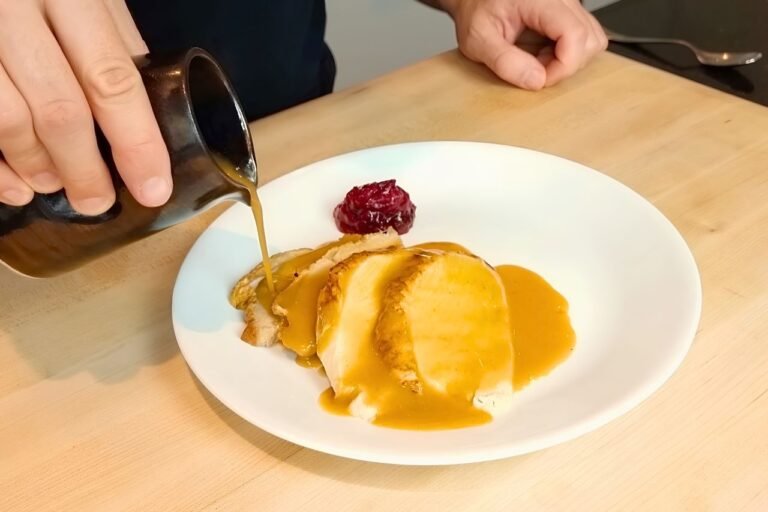 Gravy being poured from a jug over sliced turkey on a white plate with cranberry sauce