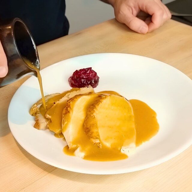 Gravy being poured from a jug over sliced turkey on a white plate with cranberry sauce