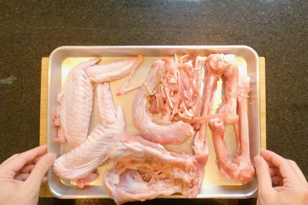Overhead view of hands holding a tray of raw turkey wings and bones