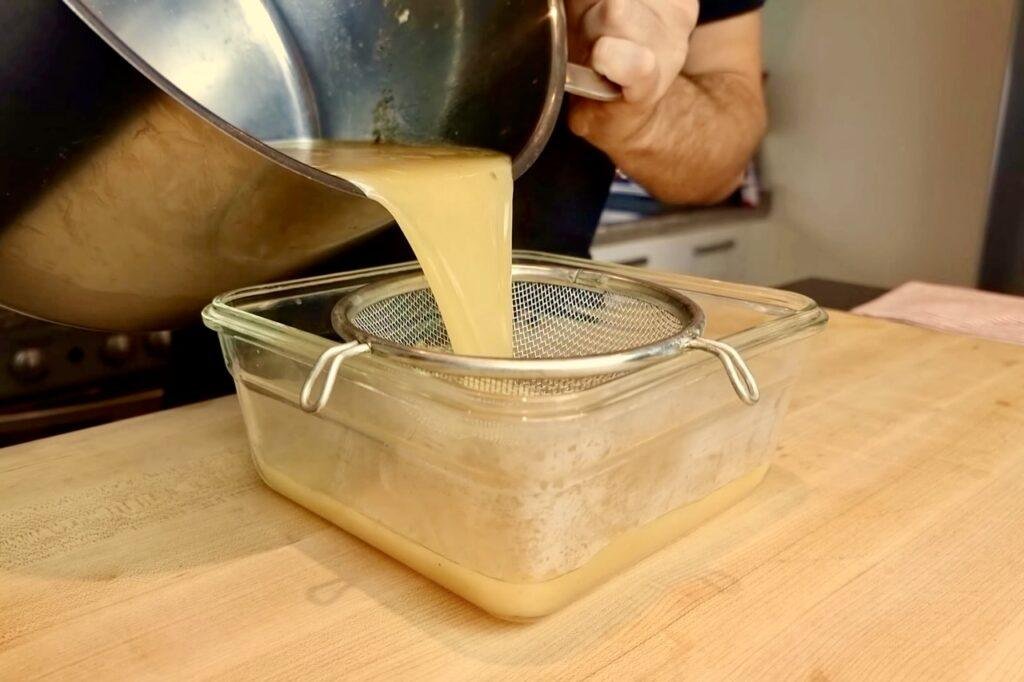 Gravy being poured through a sieve into a glass dish