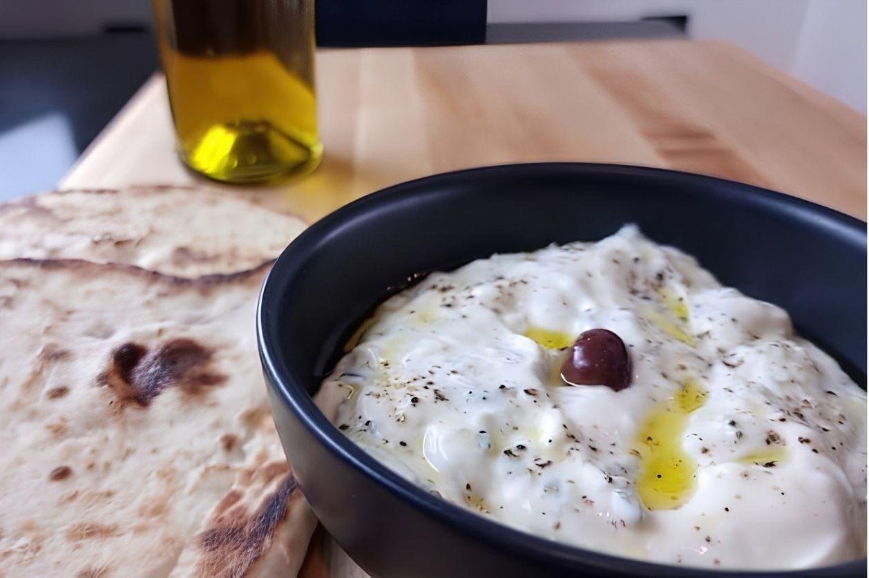 Creamy tzatziki in a bowl drizzled with olive oil, served with warm flatbreads and a bottle of olive oil in the background.