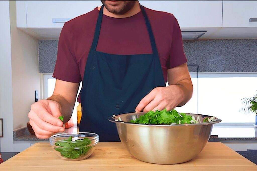 Chef adding fresh herbs to a steel bowl of shredded salad in a kitchen