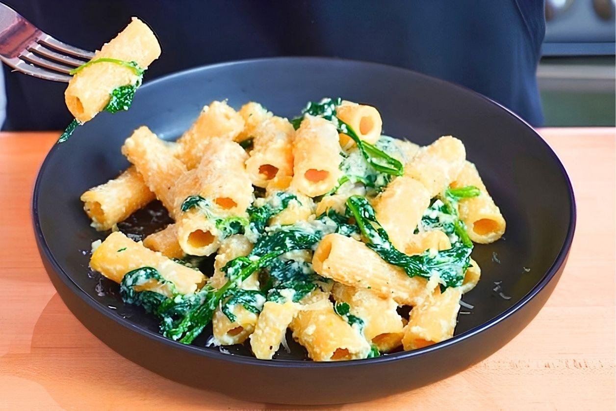Fork lifting a piece of rigatoni from a dark bowl of spinach and ricotta pasta